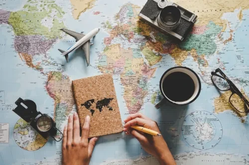 Mesa com mapa-múndi, caderno com desenho do globo, café, câmara fotográfica, bússola e avião em miniatura, simbolizando planeamento de viagens financiadas por crédito pessoal.
